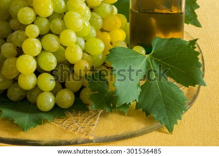 On the left grapes with leaves on a plate,  and on the right a glass of grape juice next to the grapes on the yellow background. Grapes and grape  juice. Horizontal shot. Daylight.