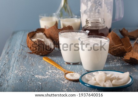Glass of Coconut Smoothies with Coconut. Coconut smoothie vith slices of fresh coconut and flakes in spoon on wooden background.