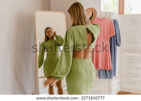 young pretty woman in green dress trying on fashion style trend dress looking in mirror at home or showroom Foto stock © 