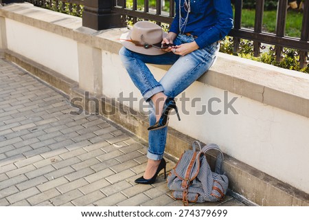 young stylish pretty woman, hands holding a phone, denim shirt and jeans, high heel shoes, hat, backpack, sunny day, good weather, city street, vacation europe, travel, detail, cool accessories