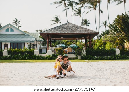 young stylish hipster couple in love walking playing dog puppy jack russell, tropical beach, cool outfit, romantic mood, having fun, sunny, man woman together, horizontal, vacation, house home villa