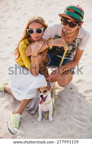 young stylish hipster couple in love walking playing dog puppy jack russell in tropical beach, sitting on white sand, cool outfit, romantic mood, having fun, sunny, man woman together, vacation