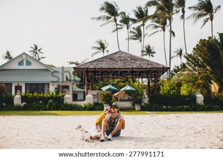 young stylish hipster couple in love walking playing dog puppy jack russell, tropical beach, cool outfit, romantic mood, having fun, sunny, man woman together, horizontal, vacation, house home villa