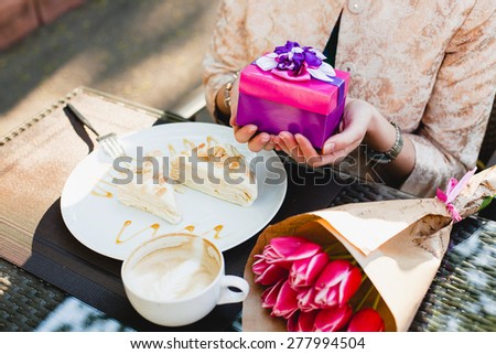 young stylish woman, sitting in cafe, holding present box, smiling, enjoying tulips, happy birthday party, city street, europe vacation, detail, close up, horizontal, glamour outfit, romantic dinner