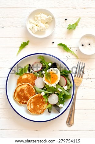 pancakes and egg salad on a light wooden surface