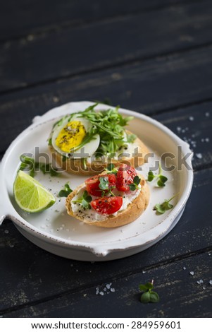 mini toast with egg, arugula and cherry tomatoes in a vintage plate on a dark background