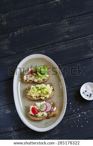 mini toast with cheese, cucumber, radish, tomatoes and egg on a dark background