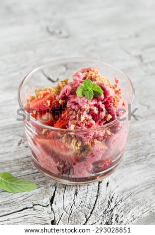 frozen yogurt with strawberries, biscuits and mint leaves in a glass beaker on a light wooden background