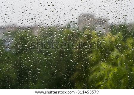 Raindrops on a window pane. Summer day. In the background buildings and trees
