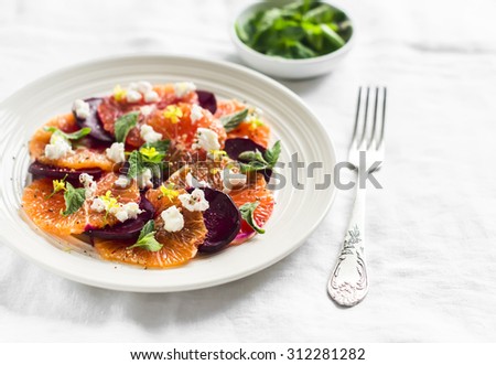 salad with beets, oranges and soft cheese on a white plate on a light surface