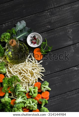 Raw ingredients - pasta, broccoli, carrots, olive oil - cooking delicious vegetarian pasta with vegetables, on a dark wooden surface