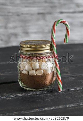 Homemade Christmas gift - ingredients for making hot chocolate with marshmallows in a glass jar on a wooden surface