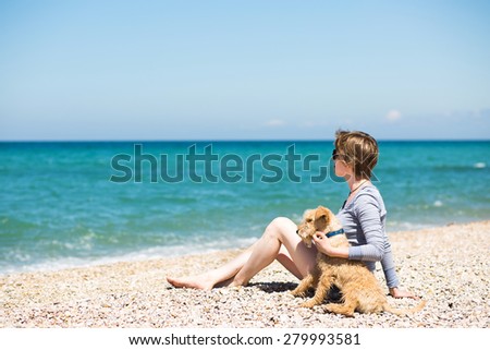 Beautiful girl with blonde hair in a blue blouse sitting on the beach with a dog
