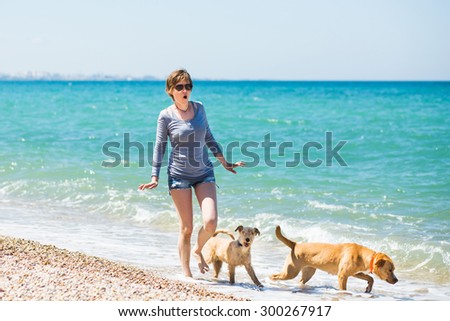 Beautiful girl in a blue blouse and shorts walking with dogs on the beach