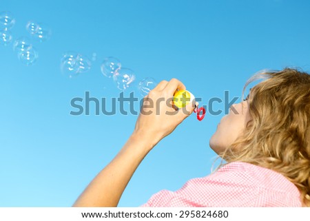 Beautiful young blonde girl blowing soap bubbles into the sky.