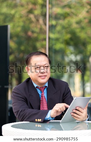 Asian senior businessman in suit using tablet outdoor