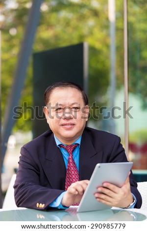 Asian senior businessman in suit using tablet outdoor