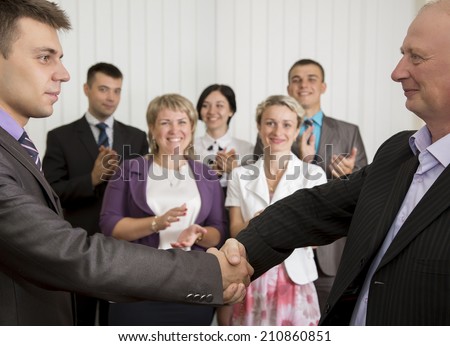 Business award. Mature businessman congratulates younger employee standing in front of the happy team