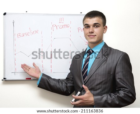Young business consultant stands at the wall drawing board and pointing out at the chart.