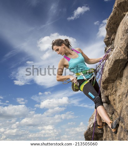 Beautiful female climber hanging on the rope and equipped with many climbing gears.