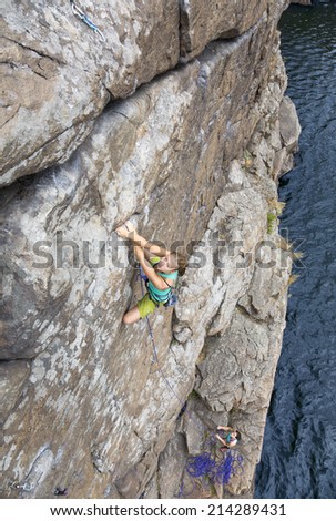 Climbing partners make ascent on to the rock wall. Two female extreme climbers ascending the vertical rock over the rocky beach.