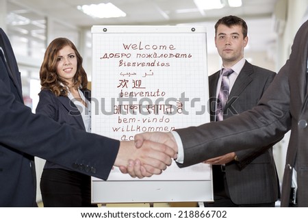 Male and female coaches welcome participants of the corporate training. They stand next to flip chart with \