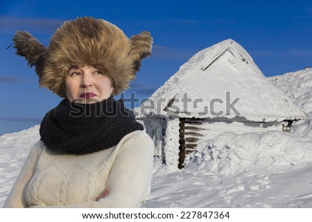 Smiling lady dressed in warm winter hat. Snowbound hut on the background
