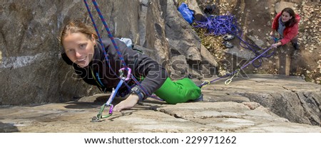 Two female rock climbers. Blond climber is leading, brunette climber is belaying. Narrow horizontal composition fits most of website headers