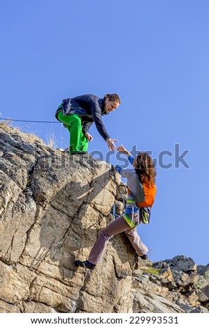 Climber helps her partner to rich the summit. Two female climbers, one drags the hand of another. Deep blue sky on the background