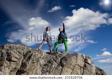 Group of two female climbers observing the surroundings from the summit. Impressive  cloudy sky and sun on the background