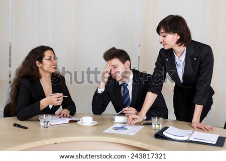 Corporate life. Annoyed and tired young male executive surrounded with two nice female assistants.