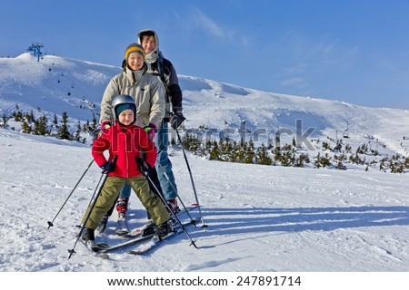 Family of three people learns skiing together. Mixed race family stays on the snow slope with the skis attached. Happy, smiling, joyful.