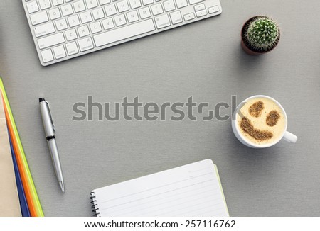 Office work space on grey desk with cactus and cappuccino. From above view on grey wooden desk with well organized office supplies and mug with cappuccino with chocolate smiley on the surface.