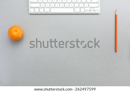 Working space in grey-orange. Creative office style composition with tangerine, keyboard and orange pencil located on grey wooden desk. Top view.