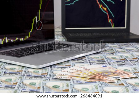 Making money.\
Desk covered with flat layer of US and European cash notes and two laptops on the background with Forex charts: bullish and bearish