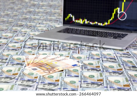Forex trading.\
Desk covered with flat layer of US and European cash notes and laptop on the background with bullish Forex chart