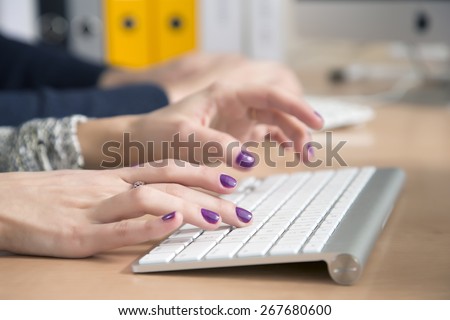 Female fingers typing on keyboard. Office desk with keyboard and some other office supplies, female palms on the foreground, male hands on the background. Fingers of lady with vivid nail make-up