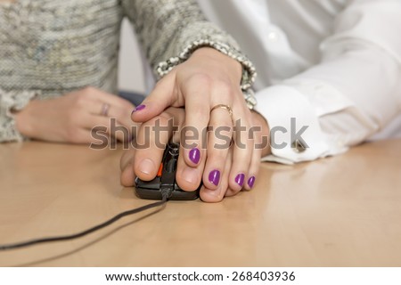 Web browsing together.\
Male and female hands keeping black computer mouse on beige wooden desk