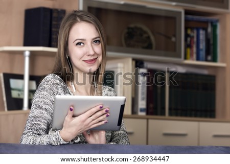 Smiling lady with electronic devise. Portrait of beautiful young woman holding tablet PC. Contemporary home interior on the background, copy space on the right side