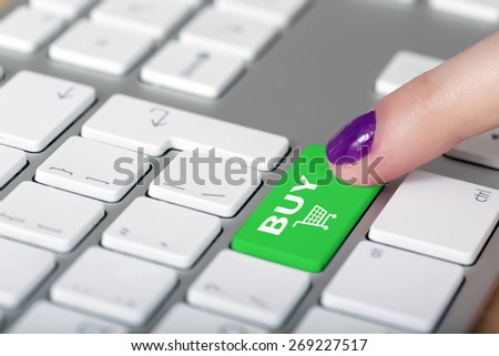 Internet shopping. Female finger clicking on BUY button on computer keyboard with white buttons but green shopping button with cart symbol