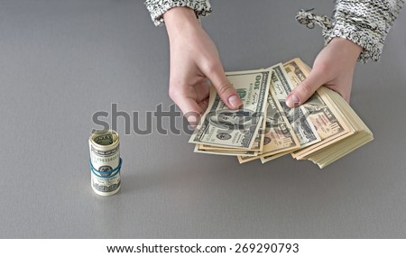 Counting large stack of cash notes. Woman hands holding stack of US cash notes and rolled tube of several notes on the left