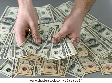 Cashier hands. Man holding larges stack of US cash notes above desk covered with layer of dollars notes of different value