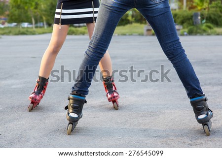 Bodies of two female skaters. Diverse dressed legs of two slim girls skating on roller skates on paved road together