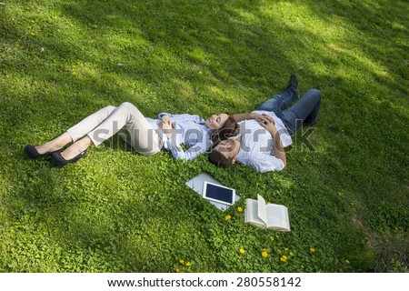 Young man and woman napping on grassy lawn. Cute young man and woman casual dress official shirt napping dreaming lie on green grass with yellow flowers laptop tablet PC book around