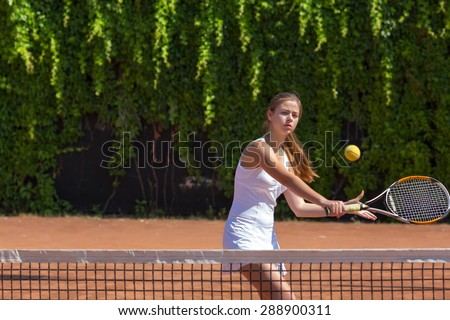 Female athlete returning ball.\
Young woman playing tennis swinging racket returning ball orange clay ground white dress with miniskirt green fence on background