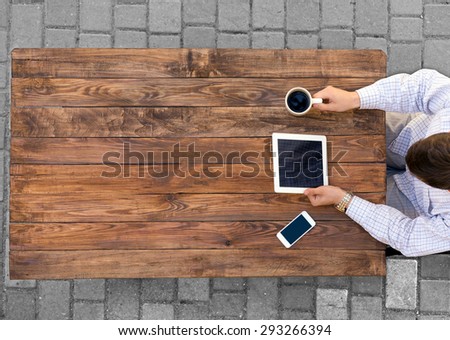 Man working at vintage rough wooden desk directly from above browsing electronic gadget drinking coffee mobile office phone paved road on background casual dress code white shirt