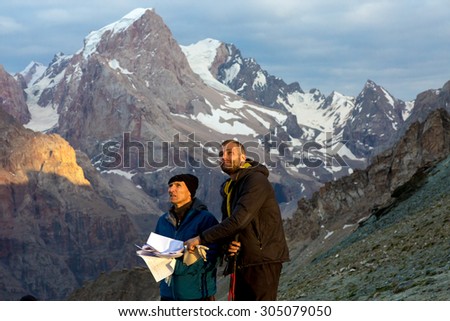 Climbers learning future route of ascent Two people old and young man discuss mountain way keeping stack of papers with route description guidebook printed faces highlighted last sunbeams warm sun