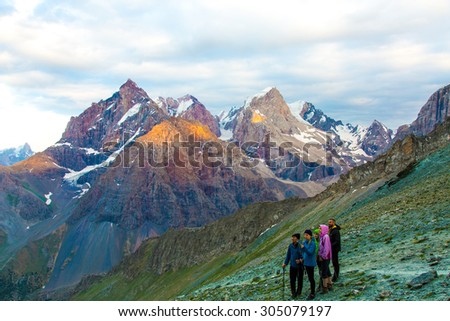 People observing mountain scenery.\
Large group of men staying on grassy trail looking side mountain peaks rocky ridge cloudy sky background