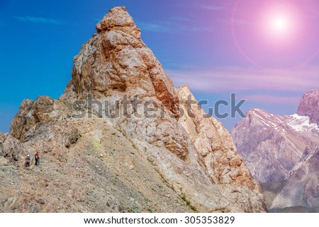Razor sharp summit and climbers. Mountain landscape and blue sky with small bodies of people moving toward rocky summit sun shining sky background