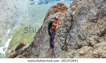 Person climbs mountain Female mountain climber traversing bright orange red rock moving towards point of shoot color mountain range and with green grass and white snow background
